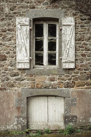 Facade of an old house with a basement hatch and a window with cobwebs