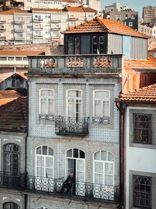 Front of a building with an elder man on his balcony watching the street below