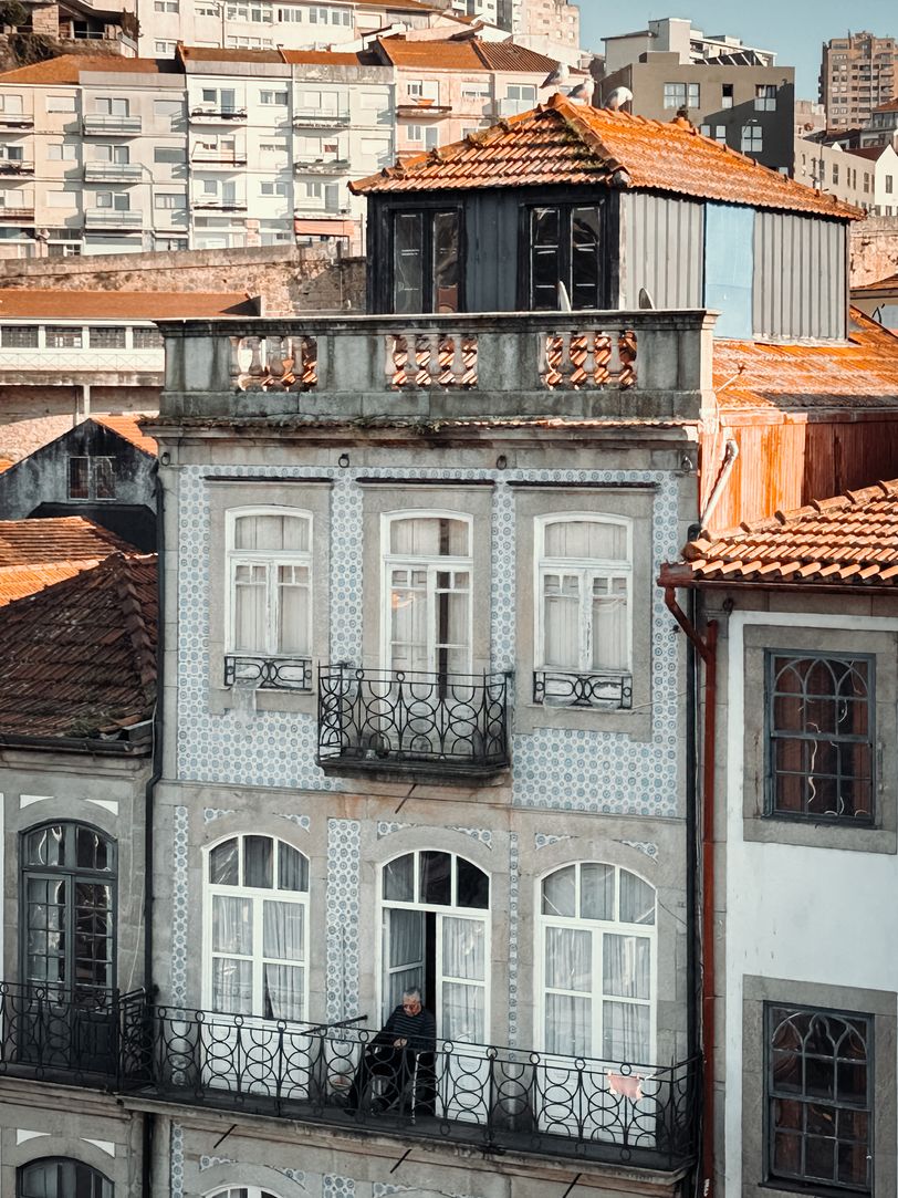 Front of a building with an elder man on his balcony watching the street below