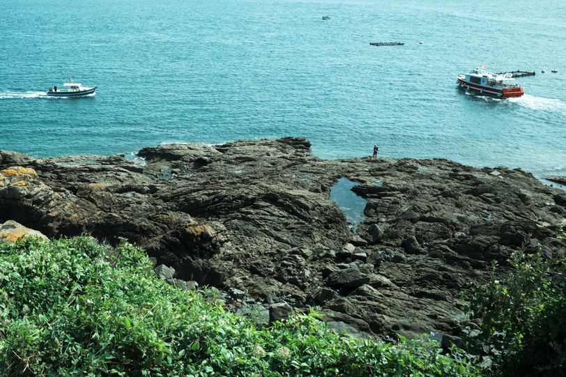 Rocky shore with boats moving and one person standing