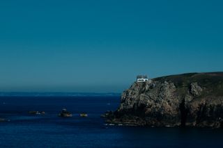 A white house at the edge of a cliff facing the sea