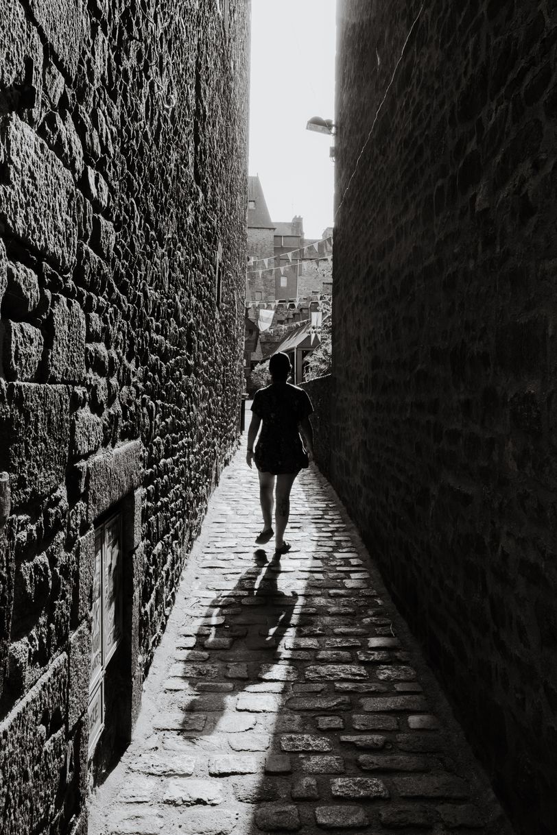 A person walking in a narrow path between buildings while facing the sun