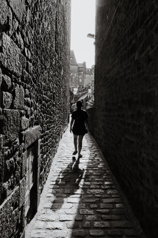 A person walking in a narrow path between buildings while facing the sun