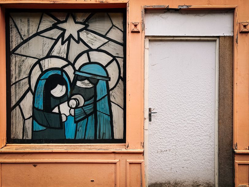 Front of an unoccupied house colorfully painted and a glass painted as painted glass showing the birth of Jesus