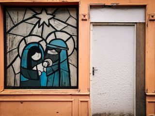 Front of an unoccupied house colorfully painted and a glass painted as painted glass showing the birth of Jesus