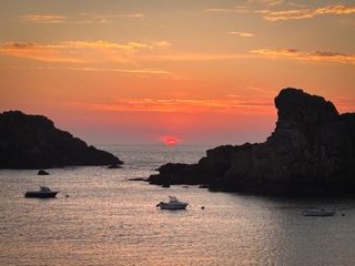 Sunset on a rocky bay with three moored boats