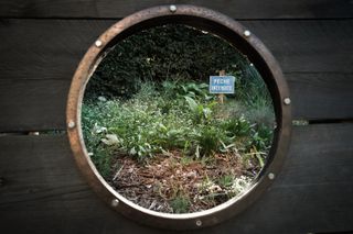 View from a porthole of a garden with a sign saying no fishing