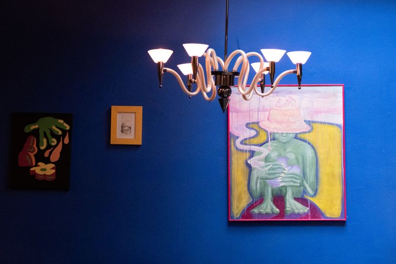 A blue wall with paintings and a crooked chandelier