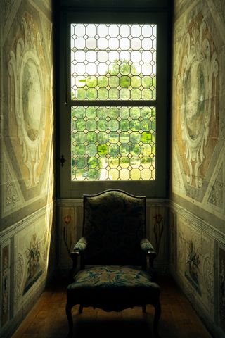 A chair with its back on the window in a narrow decorated corridor