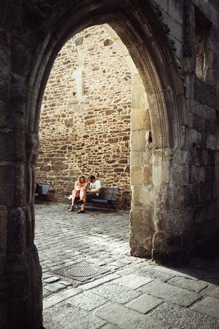 A couple resting on a bench seen through a stone arch