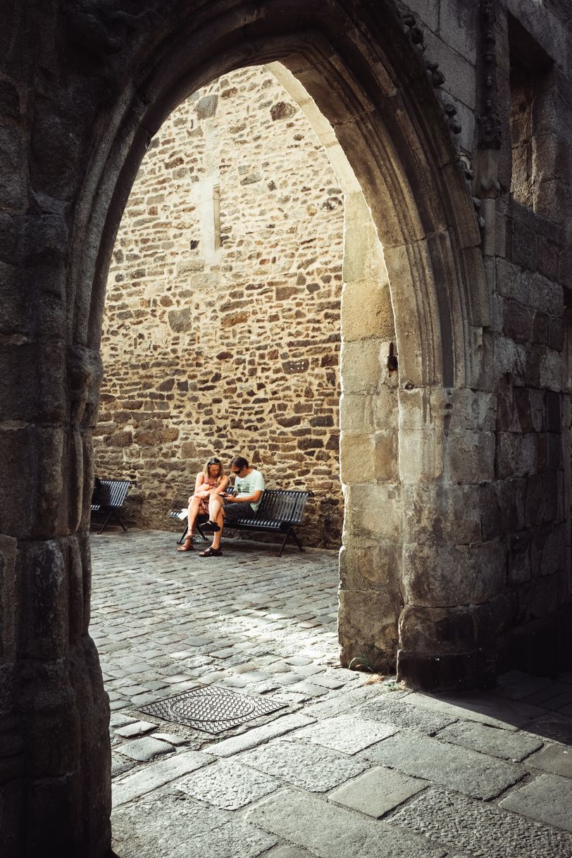 A couple resting on a bench seen through a stone arch
