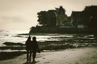 Beach at low tide with an old manor in the background and a couple walking in the foreground