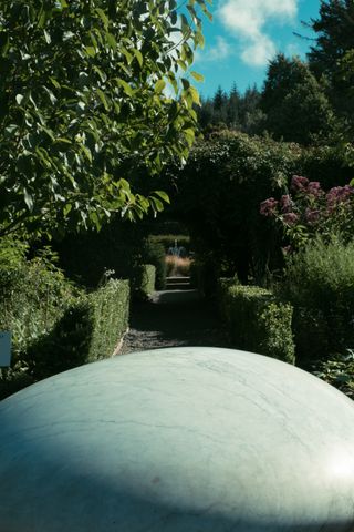 View of a passageway in a wall maintained garden with a gigantic stone in the foreground at the bottom of the picture