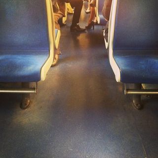 In a train wagon two legs are stepping out in the alley, one with pants and shiny dark shoes, the other with a skirt and shiny dark heels