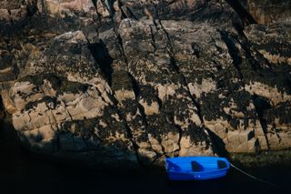 A blue boat moored at the bottom of a cliff