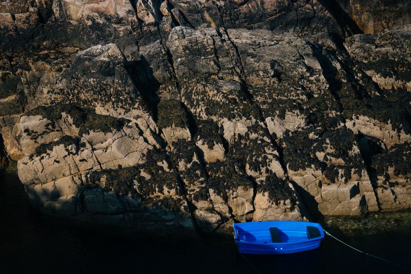 A blue boat moored at the bottom of a cliff