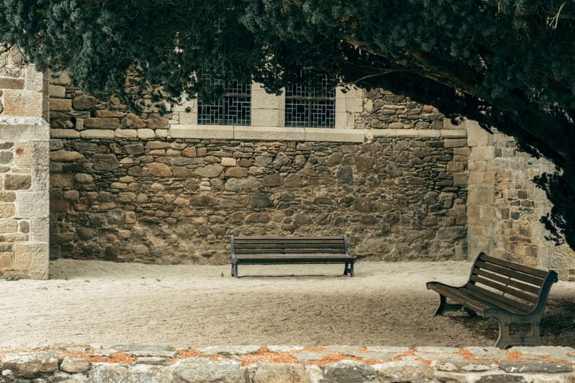 Two empty benches under a tree outside a church