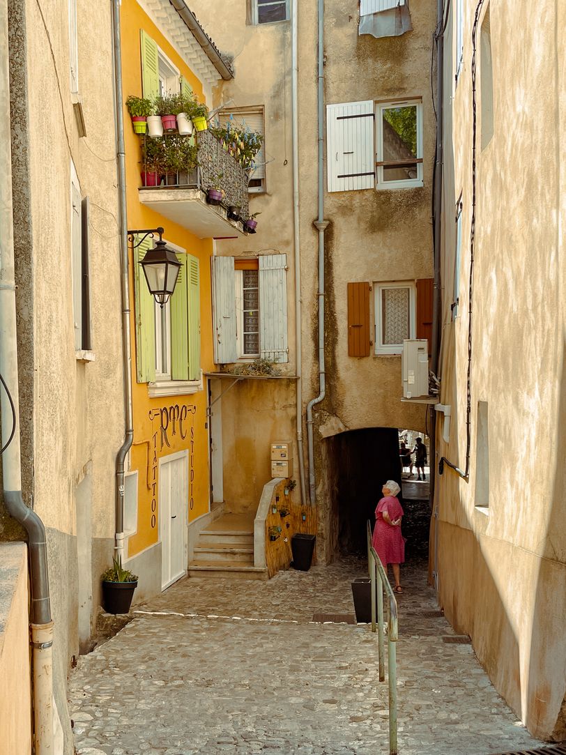 An old lady in a yellow street watching at some Tattoo shop
