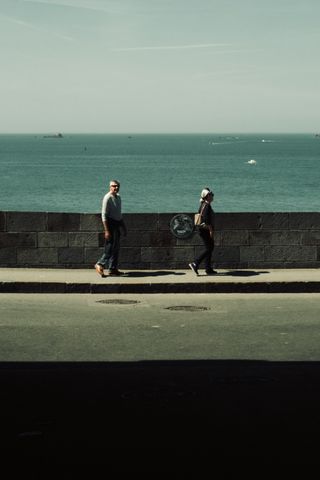 A couple walking on a road next to the sea with layers of light, colors and shadow