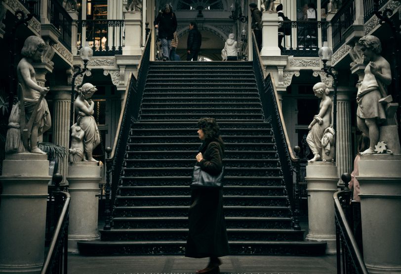A woman walking in front of stairs and surrounded by statues of standing cherubs