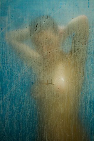 A woman taking a shower behind a steamy glass