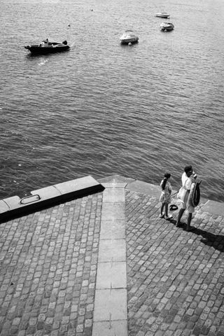 A mother and her daughter waiting on a platform while boats are passing by
