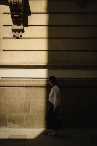 A woman walking in the street and about to get out of the shadow of a building
