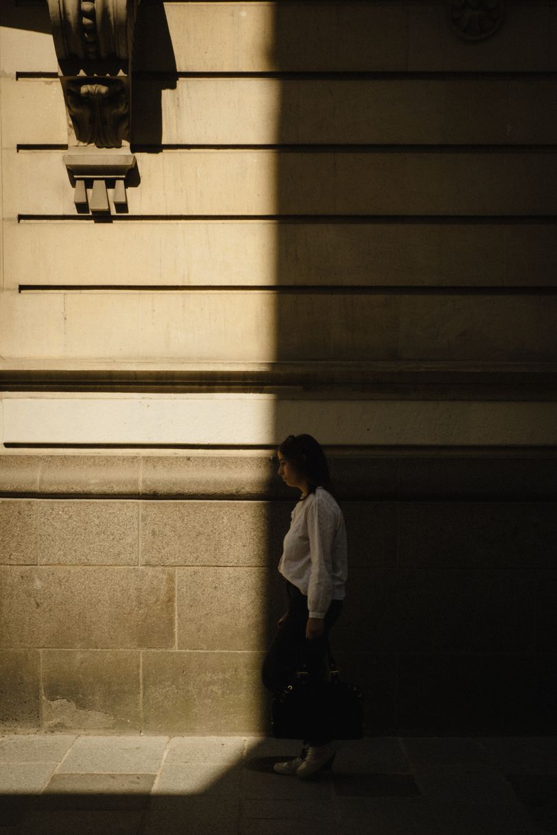 A woman walking in the street and about to get out of the shadow of a building
