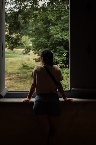 A woman in a dark room leaning through a window