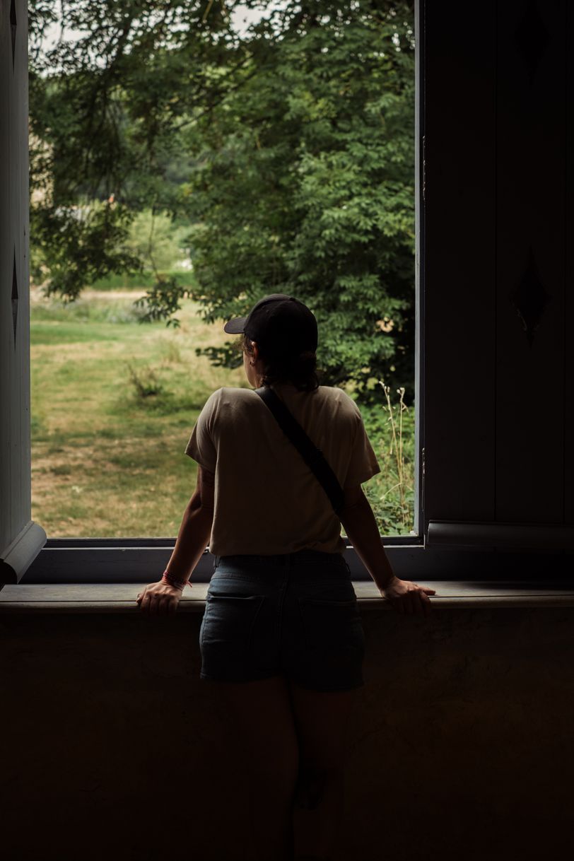 A woman in a dark room leaning through a window
